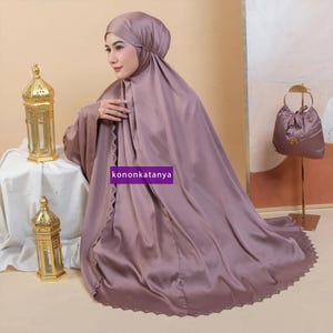May include: A mauve prayer shawl with a lace trim and a matching bag. The shawl is draped over a person's shoulders and the bag is hanging on a stand.