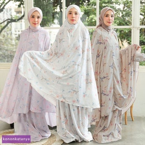 May include: Three women wearing long, flowing robes with floral and bird patterns. The robes are in shades of light purple, white, and beige. The women are wearing headscarves that match the robes.