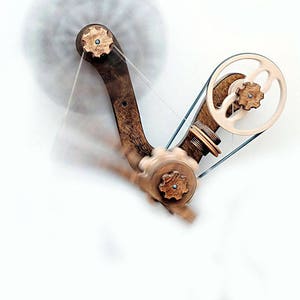 May include: A wooden spinning wheel with a brown wooden base and a white and brown wheel. The wheel is connected to a weight by a string. The wheel is spinning and the weight is swinging.