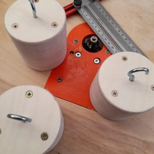 May include: Three wooden circles with hooks attached to the top. The circles are made of light wood and have a natural finish. The hooks are made of metal and are silver in color. The circles are sitting on a wooden surface.