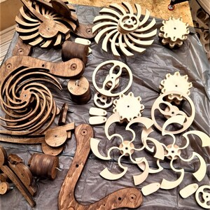 May include: A set of wooden gears and cogs in various shapes and sizes. The gears are made of light brown wood and have a natural finish. Some of the gears are in the shape of a spiral, while others are in the shape of a flower.