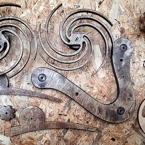 May include: A set of wooden gears and intricate wooden pieces, likely for a kinetic sculpture or art project. The pieces are arranged on a wood surface.