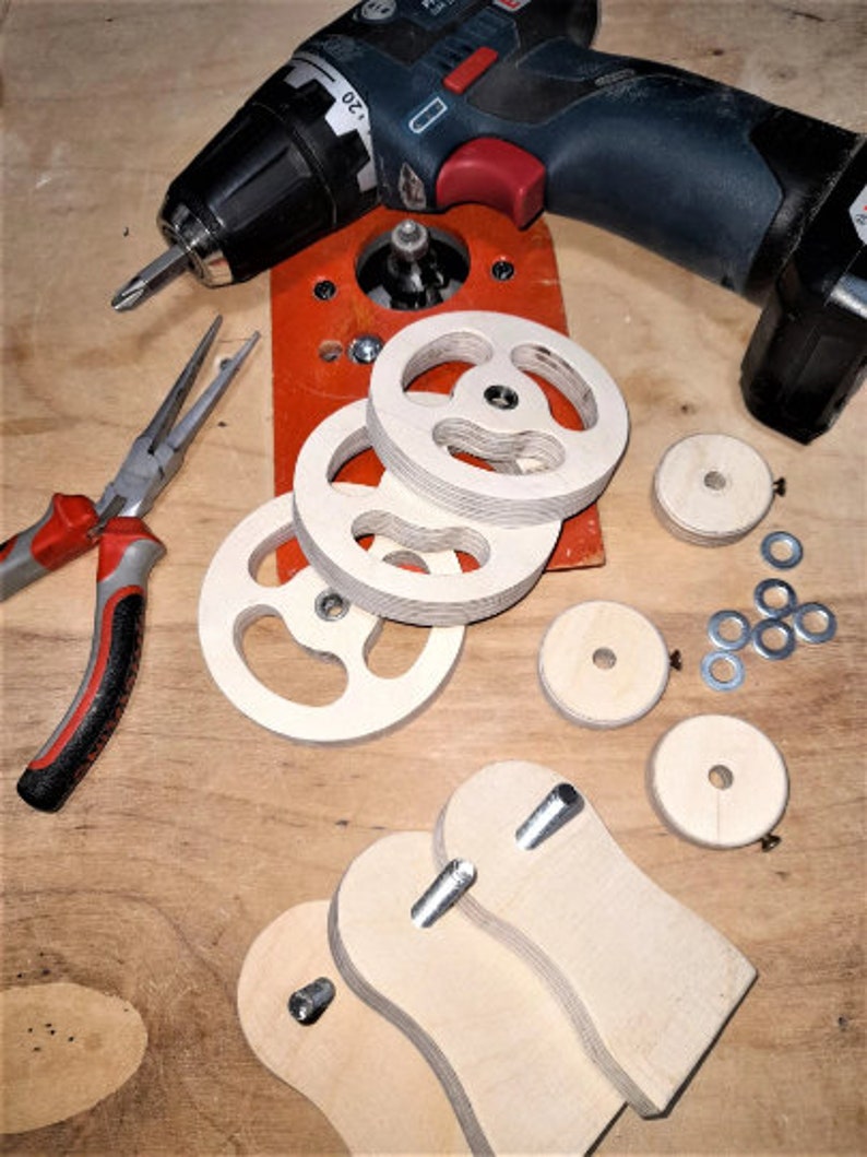 May include: A set of wooden parts for a woodworking project, including four round pieces with a center hole, two curved pieces with a hole, and a set of metal washers. The parts are laid out on a wooden surface with a drill and pliers.
