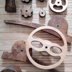 May include: A set of wooden gears and wheels, some with intricate designs, arranged on a woven bamboo surface. The set includes a large wheel with a unique, curved design, and several smaller gears with different shapes and sizes.