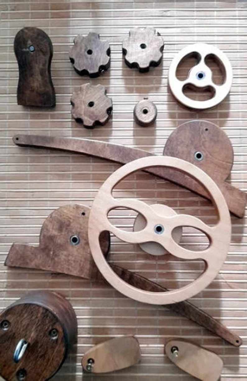May include: A set of wooden gears and wheels, some with intricate designs, arranged on a woven bamboo surface. The set includes a large wheel with a unique, curved design, and several smaller gears with different shapes and sizes.