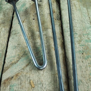 May include: Two metal hairpin legs for furniture. The legs are made of black metal and have a square plate at the top. The legs are different sizes, with the larger leg being about 16 inches long and the smaller leg being about 12 inches long.