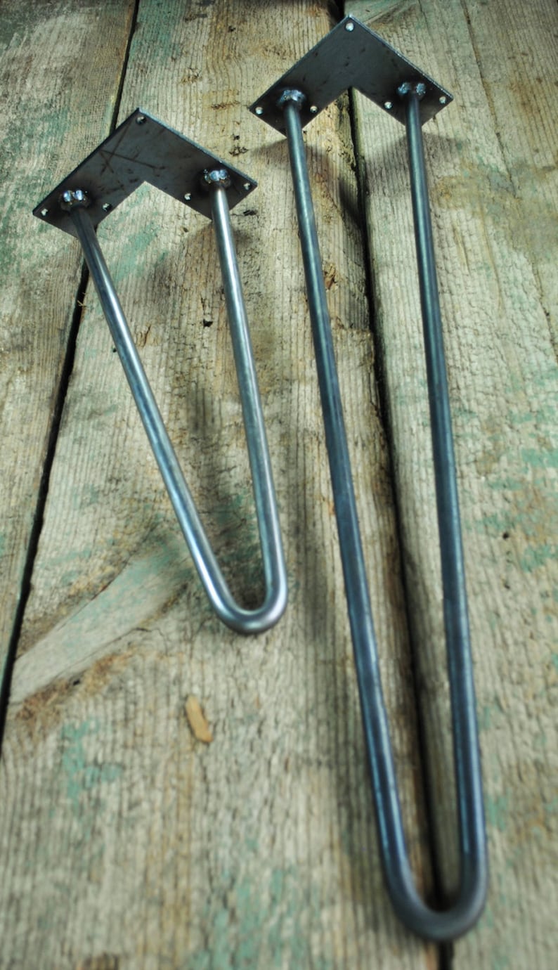 May include: Two metal hairpin legs for furniture. The legs are made of black metal and have a square plate at the top. The legs are different sizes, with the larger leg being about 16 inches long and the smaller leg being about 12 inches long.