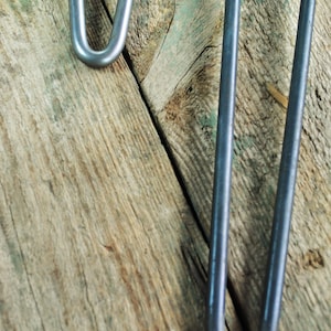 May include: Two silver metal hairpin legs for furniture, shown against a weathered wooden background.