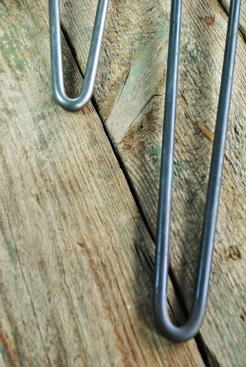 May include: Two silver metal hairpin legs for furniture, shown against a weathered wooden background.
