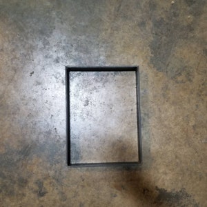 May include: A black rectangular frame is embedded in a concrete floor.