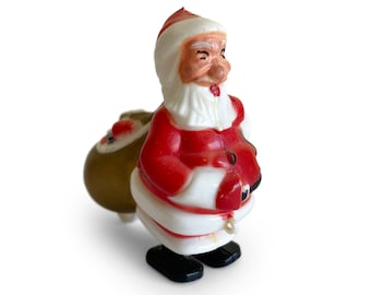 May include: A vintage plastic Santa Claus figurine with a red suit, white trim, and a white beard. He is carrying a brown sack on his back and is wearing black shoes.