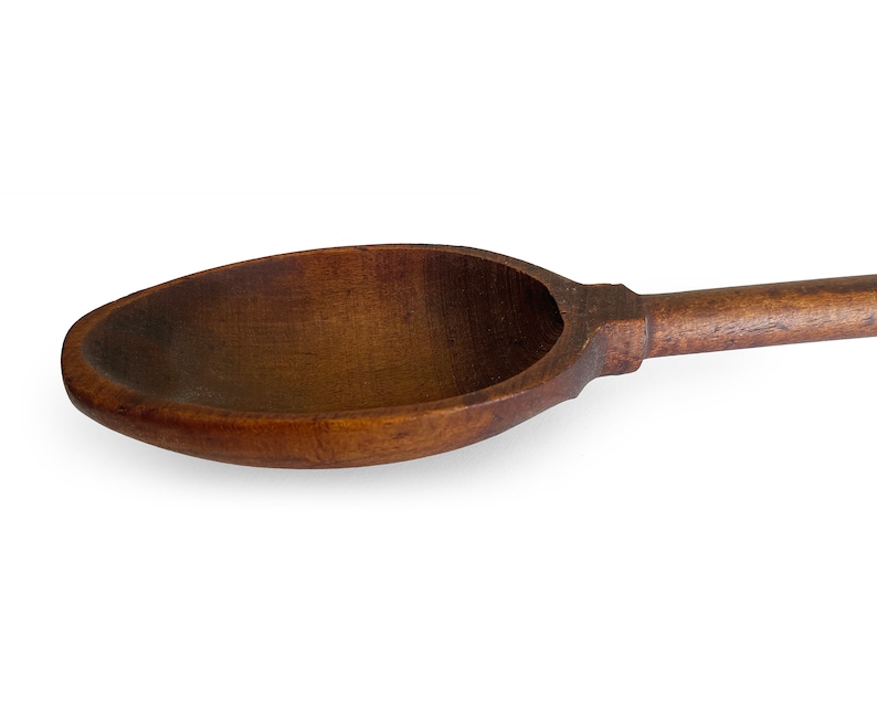 May include: A large, wooden spoon with a long handle. The spoon is made of dark brown wood and has a smooth, rounded bowl.