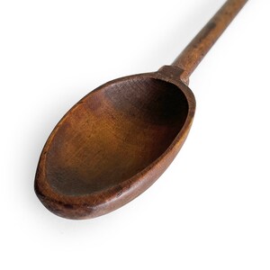 May include: A close-up of a wooden spoon with a dark brown finish. The spoon is oval-shaped and has a long handle.