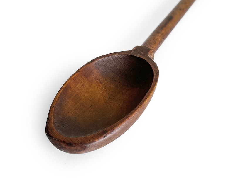 May include: A close-up of a wooden spoon with a dark brown finish. The spoon is oval-shaped and has a long handle.