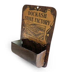 May include: A brown metal wall-mounted match holder with a sign that reads "Dockash Stove Factory Scranton, PA."