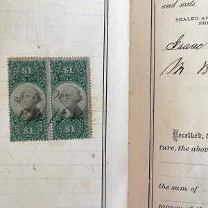 May include: Two vintage green $1 stamps featuring a portrait of George Washington. The stamps are affixed to a lined page, with a handwritten document visible on the right side. The stamps are part of a collection.