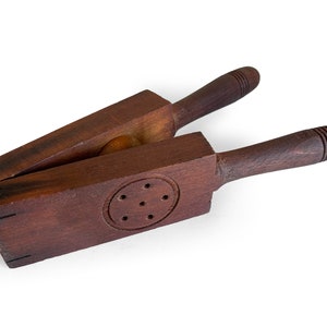 May include: A wooden cookie press with a round, carved design and two handles. The press is made of dark brown wood and has a worn, vintage look.