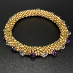 May include: A gold beaded bracelet with purple and clear gemstones.