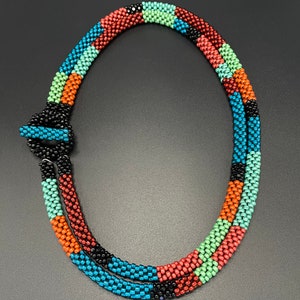 May include: A multi-colored beaded necklace with a black clasp. The necklace is made of small, round beads in shades of red, orange, green, blue, and black.