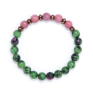 以下が含まれることがあります： 緑とピンクの宝石ビーズで作られたブレスレット。ブレスレットは、ビーズの間に銅色の金属のアクセントが施されています。