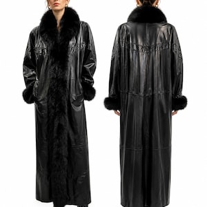 May include: A full-length black leather coat featuring a thick black fur collar and cuffs. The coat has a smooth finish with a horizontal textured panel across the upper chest and back, extending down to the sleeves. It is shown from front and back.
