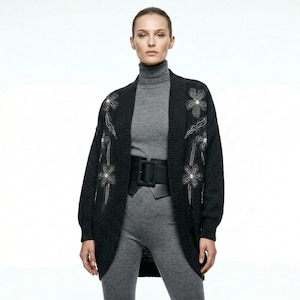 May include: A dark charcoal grey open-front cardigan featuring embroidered floral patterns with small clear embellishments on the front panels, worn over a matching grey turtleneck top and grey leggings with a wide black belt.