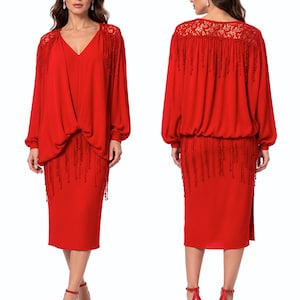 May include: A striking red dress with long sleeves and a V-neck. The dress has detailed beaded fringe on the shoulders, sleeves, and skirt. The model is wearing red strappy heels. The dress is a formal wear item.