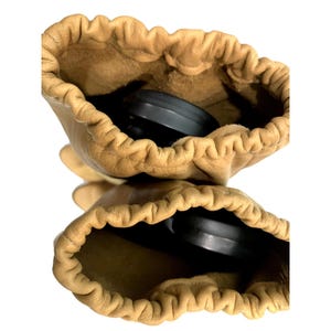 May include: Two tan leather gloves with a drawstring closure. The gloves are open, revealing a black object inside each one. The leather has a slightly wrinkled texture. The background is white.