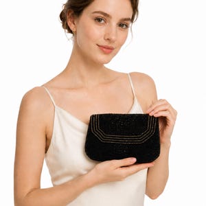 May include: A black beaded clutch bag featuring a structured rectangular shape with a flap closure. The exterior is covered in small black beads and accented with three thin, horizontal lines of gold-toned metallic beads along the flap edge.