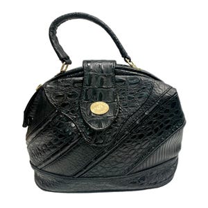 May include: Black handbag with a textured, crocodile-like pattern. The bag features a rounded shape, a top handle, and a flap closure with a gold-colored emblem. The design includes diagonal stitching and a structured base.