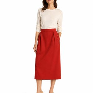 May include: A long-sleeved cream-colored crew neck sweater paired with a high-waisted, solid red midi skirt featuring subtle pleats at the waistline and a straight silhouette that falls below the knees, worn with neutral-toned pointed-toe heels.