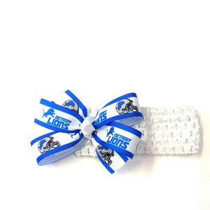 May include: White crocheted headband with a blue and white bow. The bow features the Detroit Lions logo and text. The headband is a soft, stretchy material, perfect for babies and toddlers.
