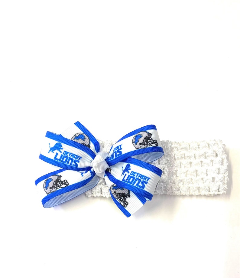 May include: White crocheted headband with a blue and white bow. The bow features the Detroit Lions logo and text. The headband is a soft, stretchy material, perfect for babies and toddlers.