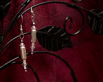 Peut inclure: Une paire de boucles d'oreilles en argent avec des accents de cristal transparents suspendus à un support en métal noir. Les boucles d'oreilles sont en forme de petits cylindres avec un cristal en haut et en bas.