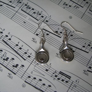 May include: A pair of silver earrings with a unique design. Each earring features a small, round, open-faced pendant with a silver finish.