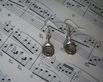 Peut inclure: Une paire de boucles d'oreilles en argent avec un design unique. Chaque boucle d'oreille présente un petit pendentif rond ouvert avec une finition argentée.