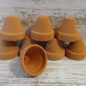 May include: A collection of small, terracotta-colored clay pots. The pots have a classic, tapered shape with a slightly flared rim. They are stacked and arranged, showcasing their simple, rustic design. Ideal for small plants or crafts.