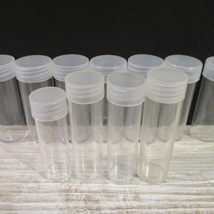 May include: A set of 11 clear plastic coin tubes with screw-on lids. The tubes are all the same size and are arranged in a row on a wooden surface.