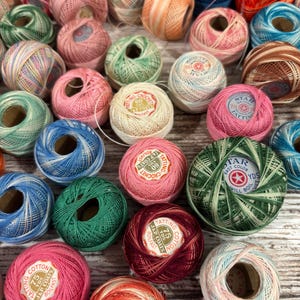 May include: A collection of colorful spools of tatting cotton in various shades of pink, green, blue, orange, and brown. The spools have labels with text including "TATTING" and "J&P COATS".