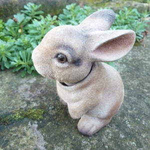 May include: A small, brown, plush rabbit figurine with a long, floppy ear. The rabbit is sitting on a gray, textured surface.