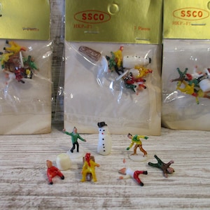 May include: A set of seven plastic figurines depicting a snowman and people in winter clothing. The figurines are packaged in a clear plastic bag with a gold header card that reads "SSCO HKP-FI 7 Pieces".