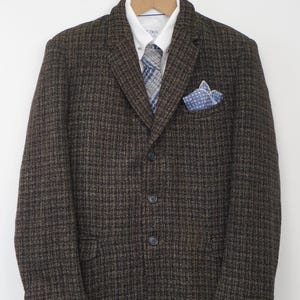 May include: A brown tweed blazer with a white dress shirt, patterned tie, and pocket square. The blazer has a classic three-button closure and is hanging on a wooden hanger.