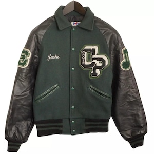 Könnte beinhalten: Eine grüne Woll-Varsity-Jacke mit schwarzen Lederärmeln. Die Jacke hat ein "CP"-Logo auf der linken Seite und das Wort "Choir" darüber. Der rechte Ärmel hat eine Musiknote und das Wort "Music" darüber. Die Jacke hat einen schwarzen und grünen Streifen an Bund und Ärmel. Die Jacke hat einen Namen "Jackie", der auf der linken Seite der Brust gestickt ist.