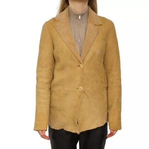 May include: A tan suede jacket with a shearling collar and two button closures. The jacket has a slightly asymmetrical hemline.