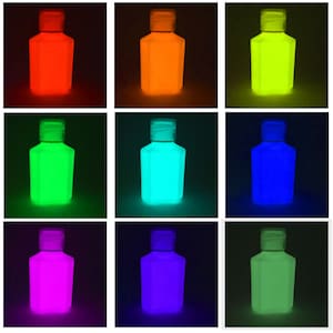 Könnte beinhalten: Neun kleine Plastikflaschen gefüllt mit leuchtender Flüssigkeit in verschiedenen Farben, darunter Rot, Orange, Gelb, Grün, Blau, Lila und Hellgrün. Die Flaschen sind in einem 3x3-Raster vor einem schwarzen Hintergrund angeordnet.