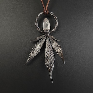May include: A silver pendant necklace featuring a clear quartz crystal set in a twisted wire circle, with a stylised silver cannabis leaf design hanging below.