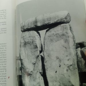Puede incluir: Fotograf&iacute;a en blanco y negro de Stonehenge, con dos grandes piedras verticales que sostienen una piedra horizontal. La imagen captura la textura erosionada del monumento y el espacio entre las piedras. El texto en la parte superior dice "Stones 57, 58 and 158 after re-erection in 1958."
