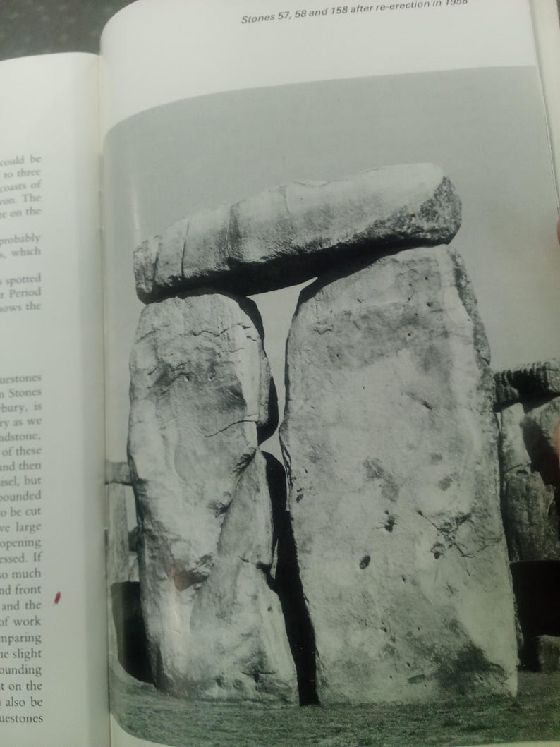 Puede incluir: Fotograf&iacute;a en blanco y negro de Stonehenge, con dos grandes piedras verticales que sostienen una piedra horizontal. La imagen captura la textura erosionada del monumento y el espacio entre las piedras. El texto en la parte superior dice "Stones 57, 58 and 158 after re-erection in 1958."