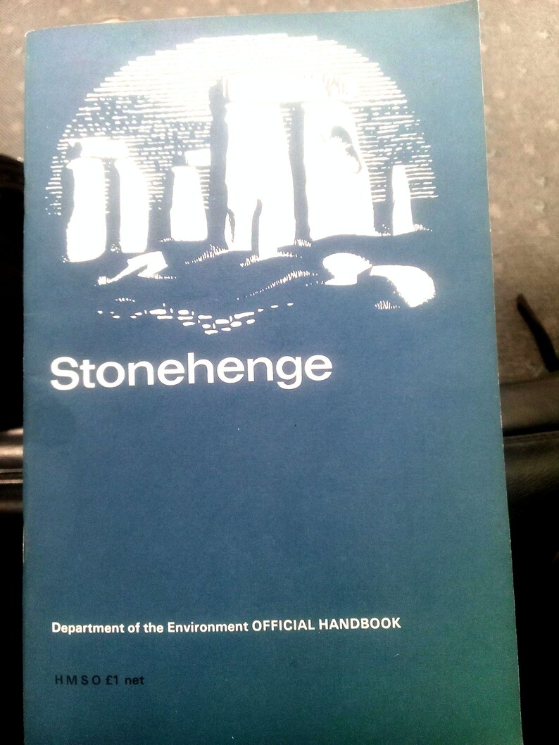 Puede incluir: Un folleto azul con la palabra "Stonehenge" en blanco. La portada presenta una ilustraci&oacute;n blanca del monumento de Stonehenge bajo un arco blanco. El texto "Department of the Environment OFFICIAL HANDBOOK" est&aacute; debajo.