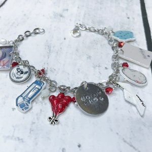Puede incluir: Un brazalete de plata con varios dijes, incluyendo un dije de globo rojo, un dije con el texto "Always", un dije con una imagen de un inhalador rojo y un dije con una imagen de un conejo blanco.